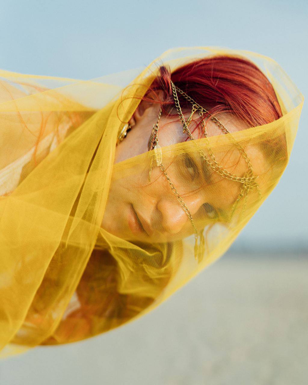Portrait of person with red hair wearing gold headchain under yellow veil